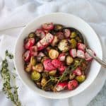 Roasted radishes and brussels sprouts in a white bowl with a serving spoon.