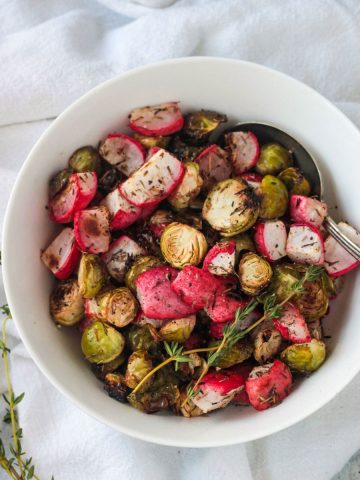 Roasted radishes and brussels sprouts in a white bowl with a serving spoon.