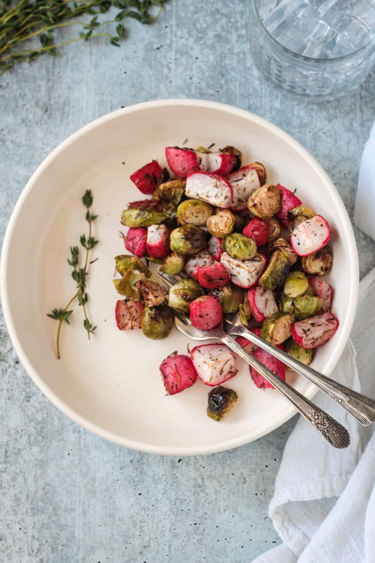 Roasted veggies on a white plate garnished with fresh thyme sprigs.