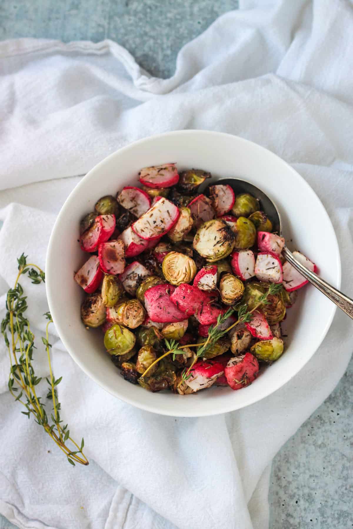 Oven roasted radishes and brussels sprouts in a white bowl with a serving spoon.