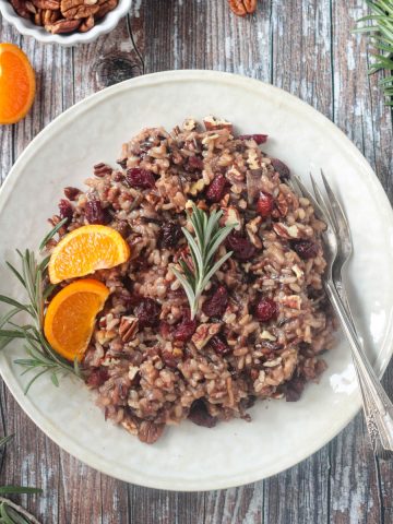 Thanksgiving rice with cranberries, citrus, and rosemary on a cream colored plate.