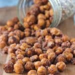 Cinnamon sugar chickpeas spilling out of a jar on a wooden board.