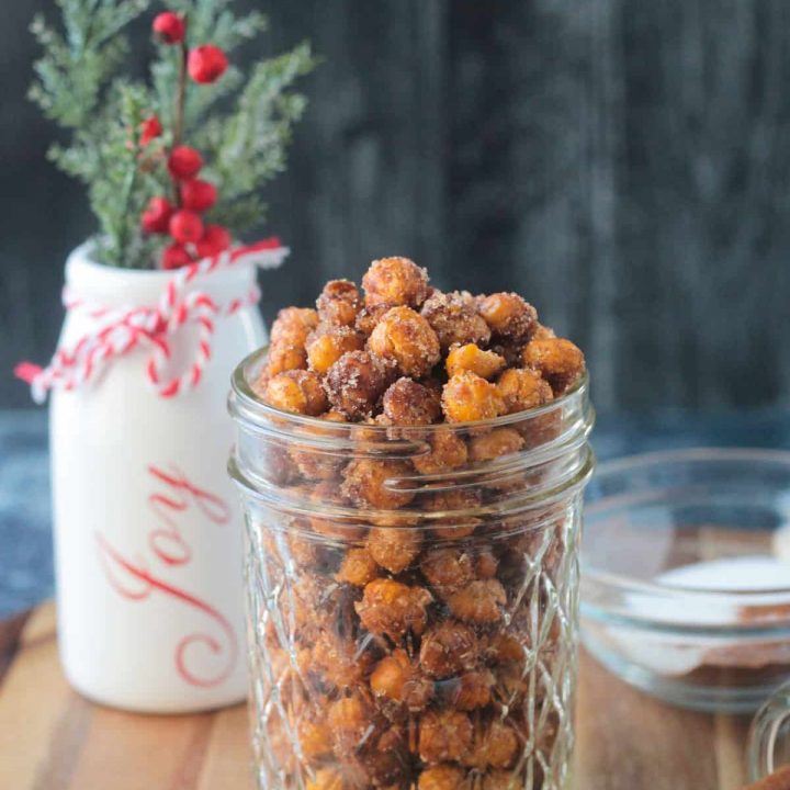 Cinnamon sugar crunchy chickpeas in a glass jar in front of a holiday vase.