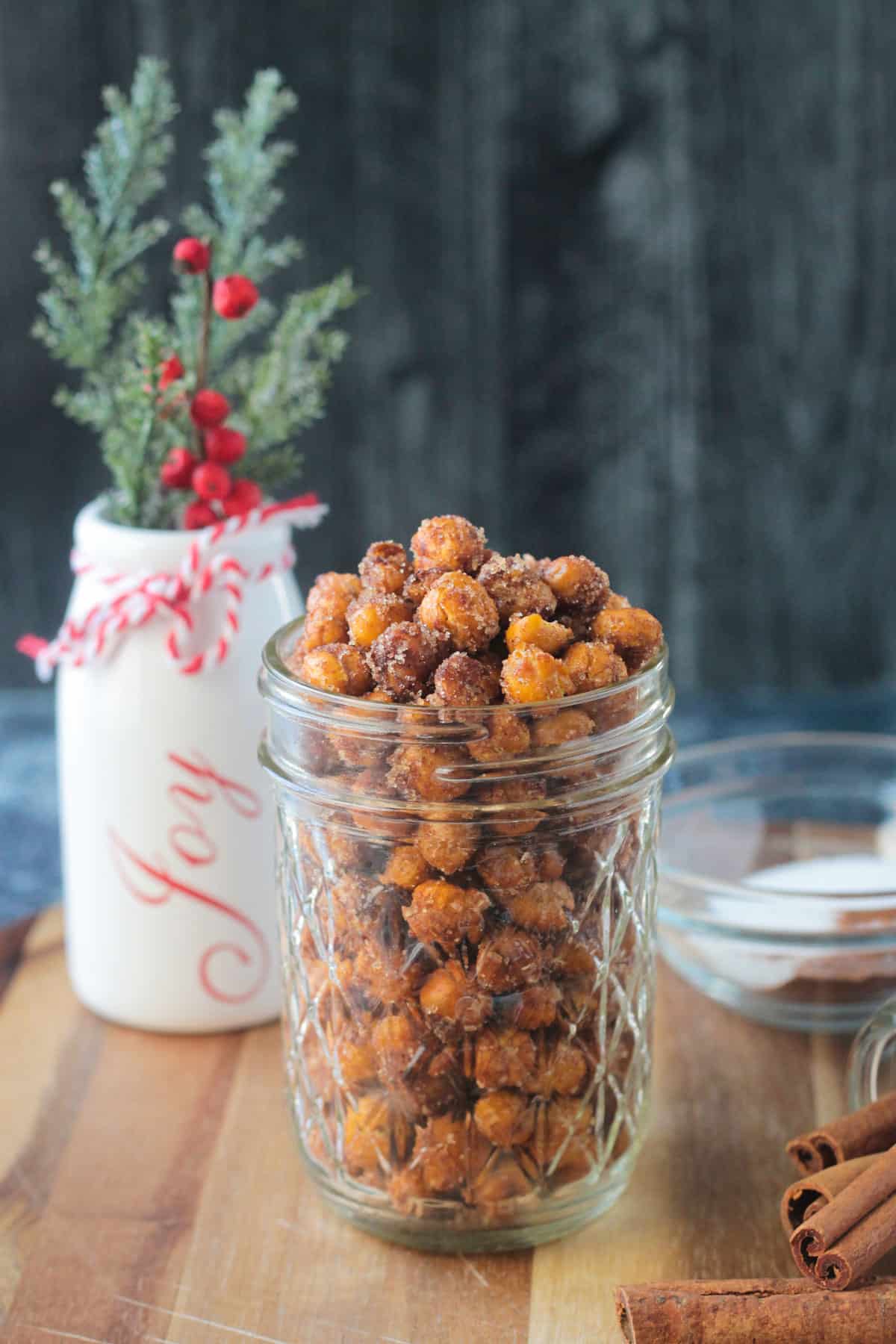 Cinnamon sugar crunchy chickpeas in a glass jar in front of a white vase.