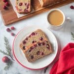 Two slices of vegan cranberry bread on a white plate next to a cup of coffee.