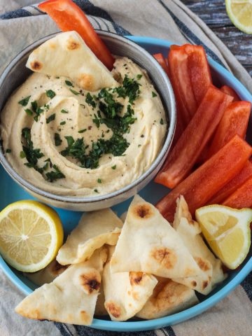 Bowl of hummus next to pita triangles and red bell pepper strips.