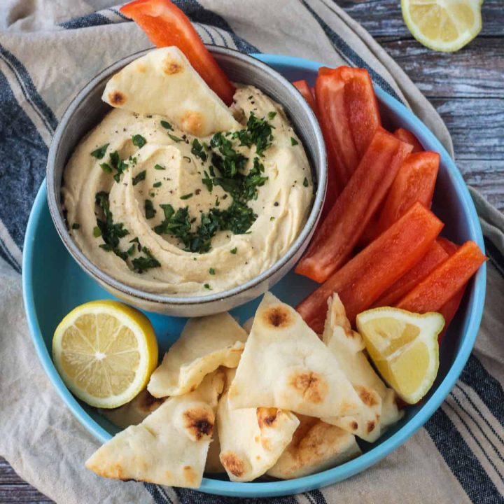 Bowl of hummus next to pita triangles and red bell pepper strips.