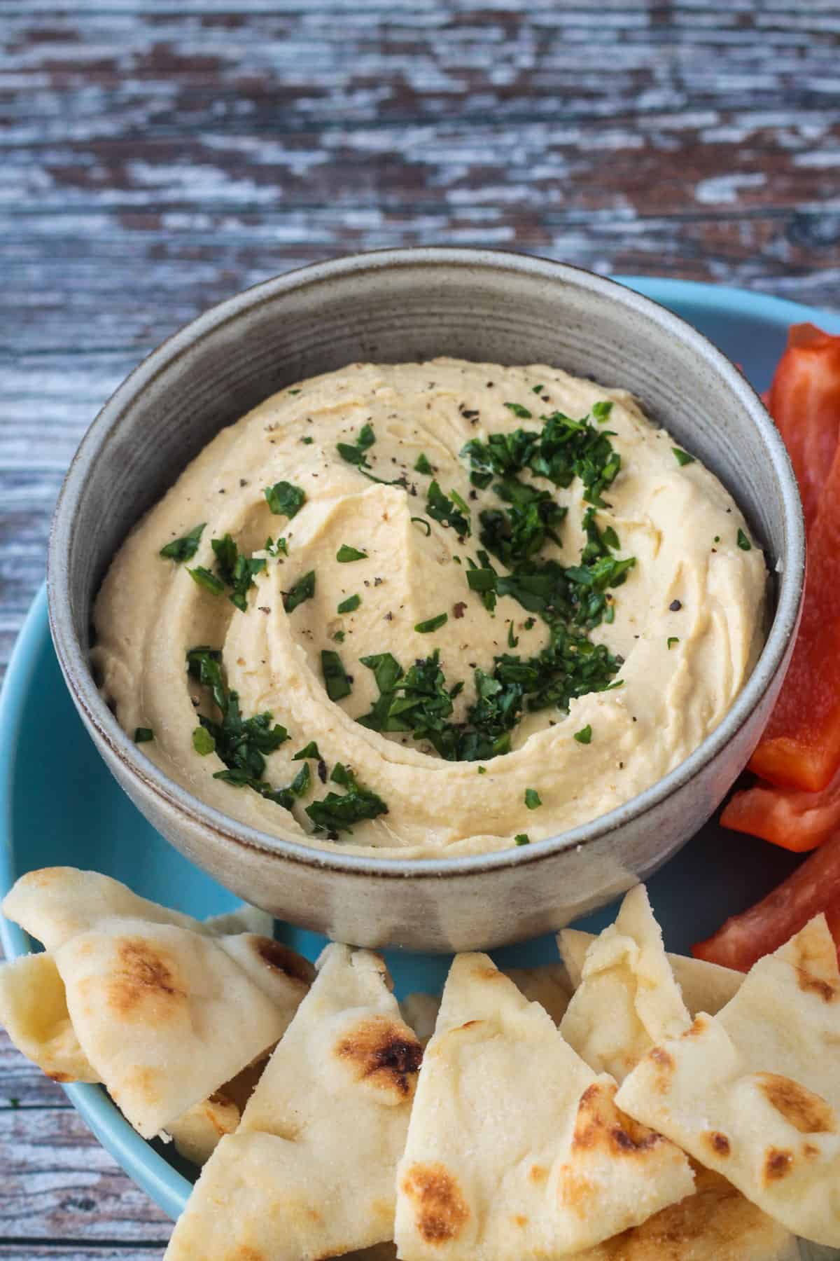 Creamy oil free hummus topped with fresh chopped parsley in a gray bowl.