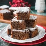 Stack of several gingerbread cake squares on a white plate dusted with powdered sugar.