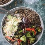 Lentils, coleslaw, roasted broccoli, and bbq sauce in a gray flat bowl.