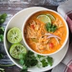 Red Curry Thai Noodle Soup in a white bowl next to two lime halves and cilantro leaves.