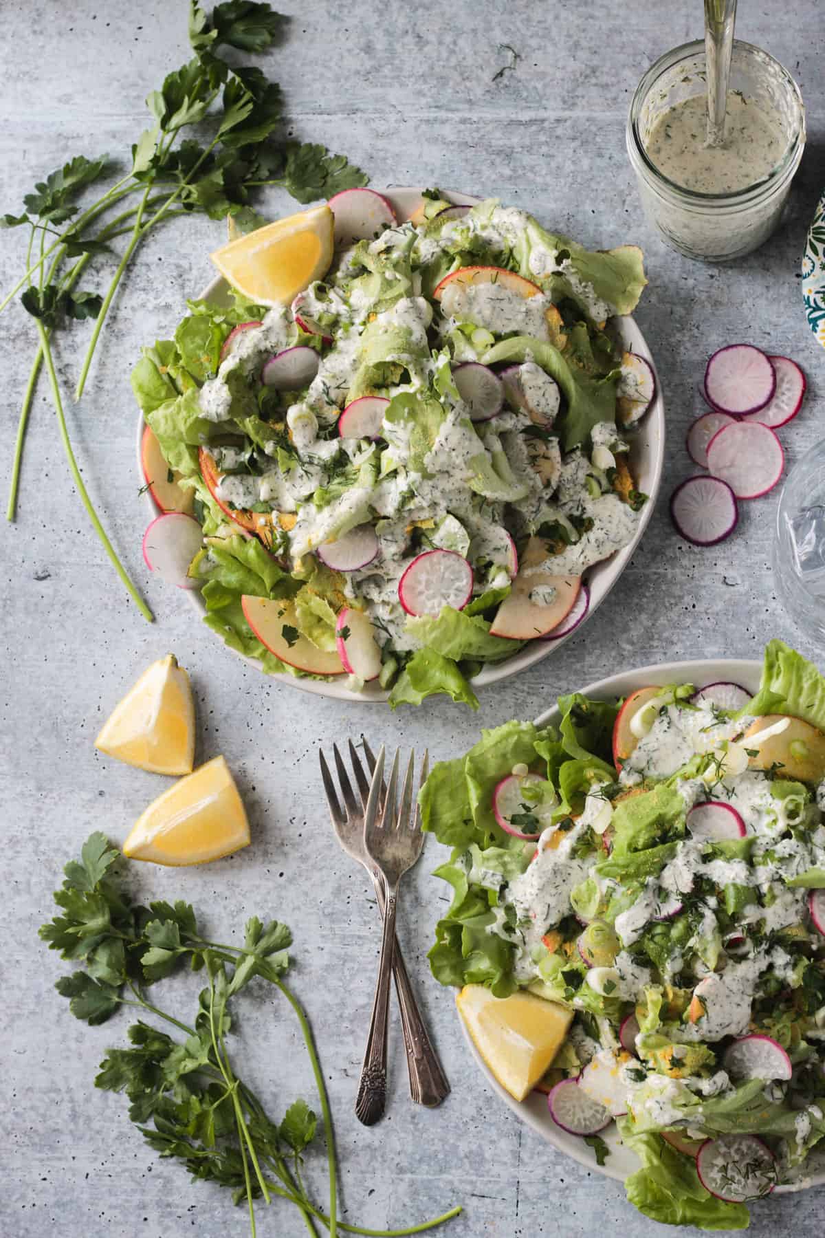 Plate of salad with apples and radishes drizzled with ranch dressing.