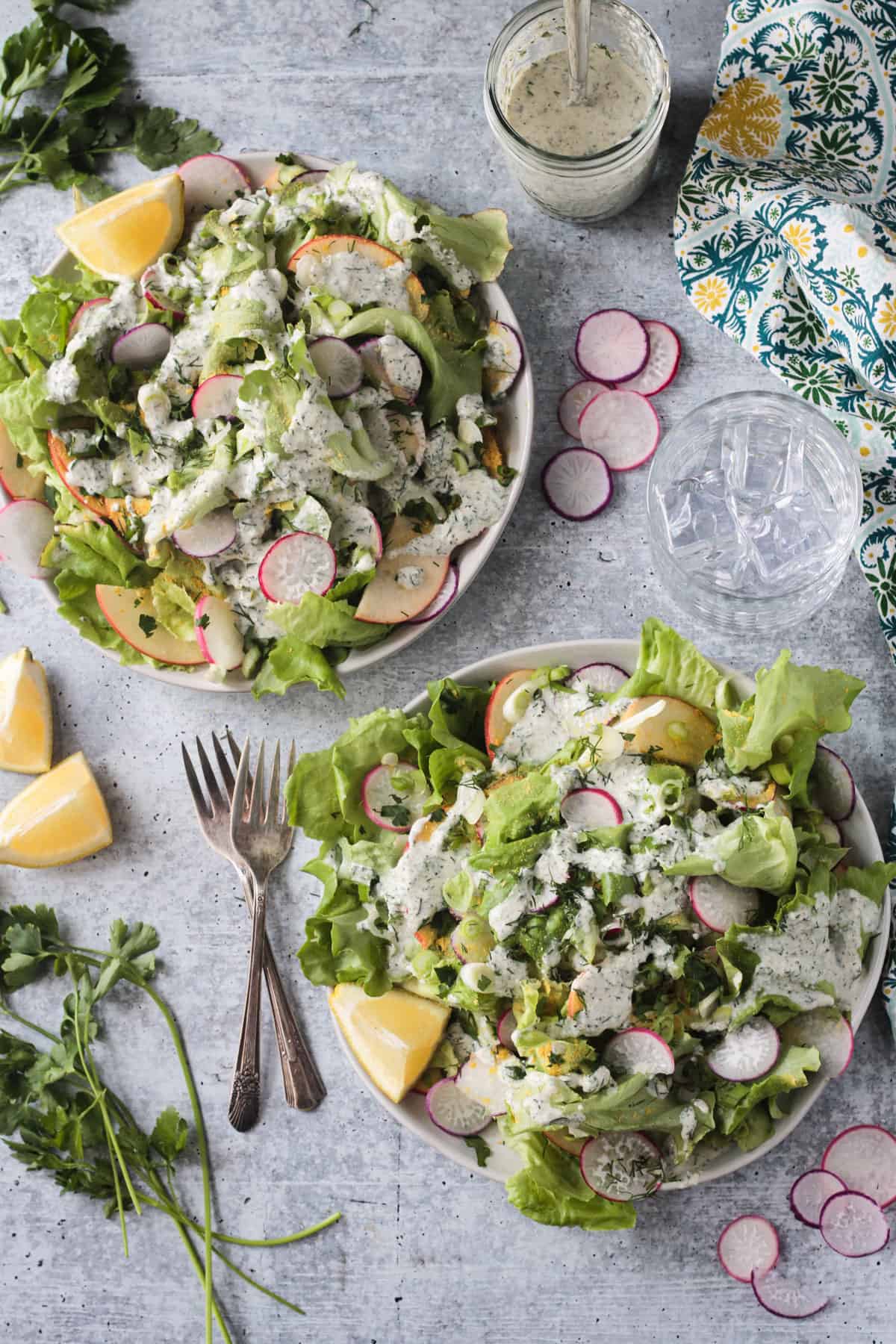 Two plates of butter lettuce salad with apples, radishes, herbs, and ranch.