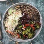 Lentils, coleslaw, roasted broccoli, and bbq sauce in a gray flat bowl.