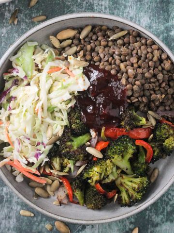 Lentils, coleslaw, roasted broccoli, and bbq sauce in a gray flat bowl.