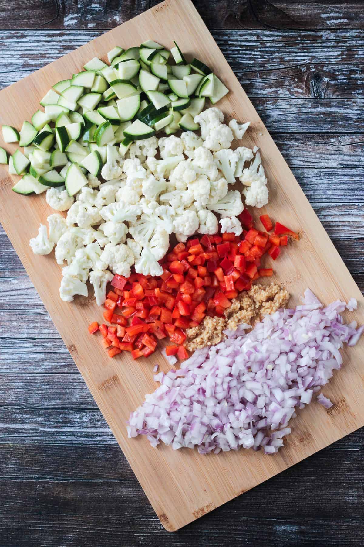 Chopped zucchini, cauliflower, bell pepper, garlic, ginger, and onion on a cutting board.
