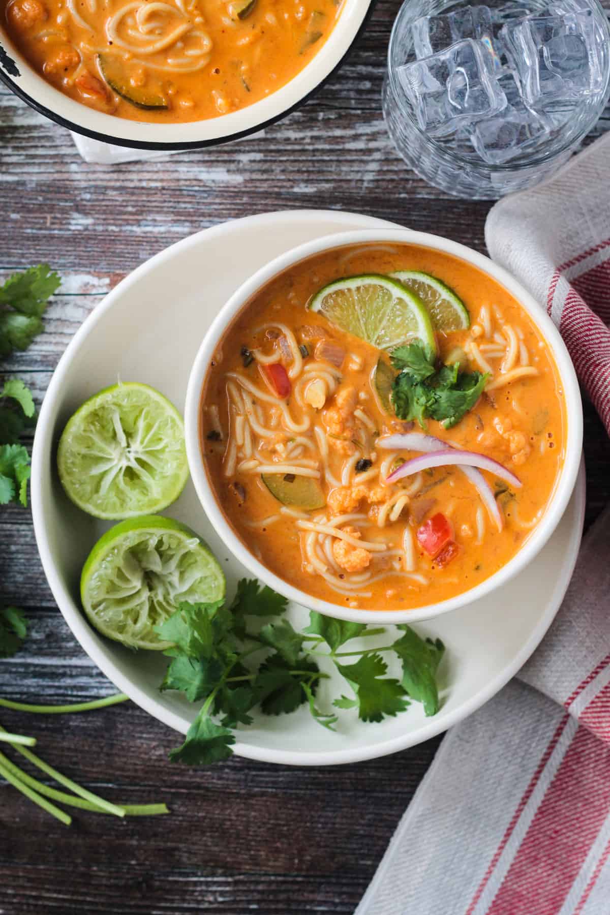 Red Curry Thai Noodle Soup in a white bowl next to lime halves and cilantro.