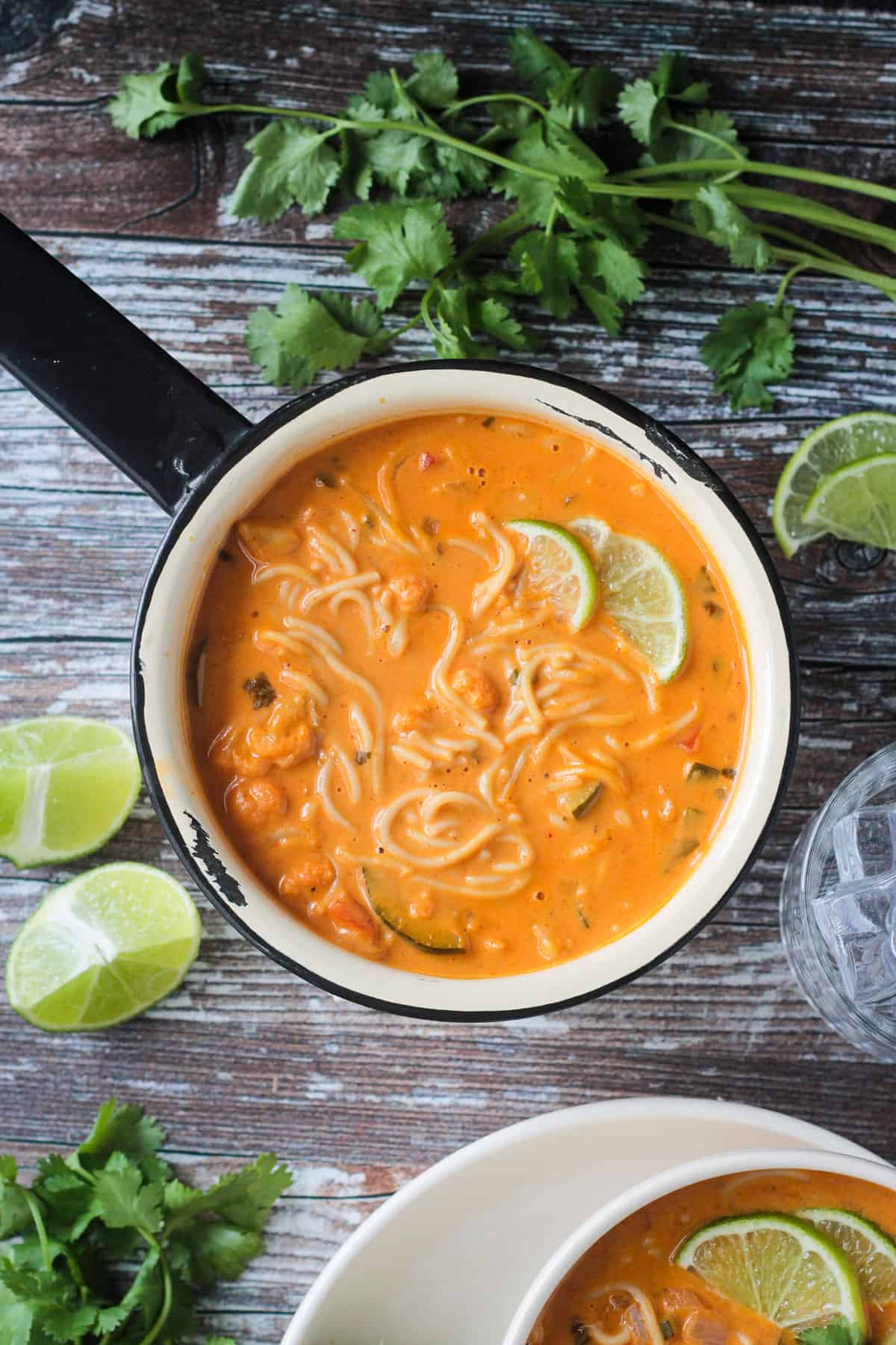 Finished red curry Thai noodle soup in a pot with lime wedges.