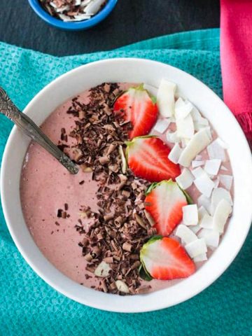 Strawberry smoothie bowl topped with sliced strawberries, coconut flakes, and chocolate shavings.