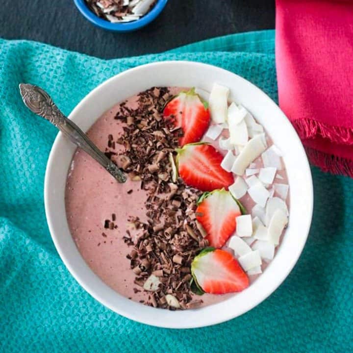 Strawberry smoothie bowl topped with sliced strawberries, coconut flakes, and chocolate shavings.