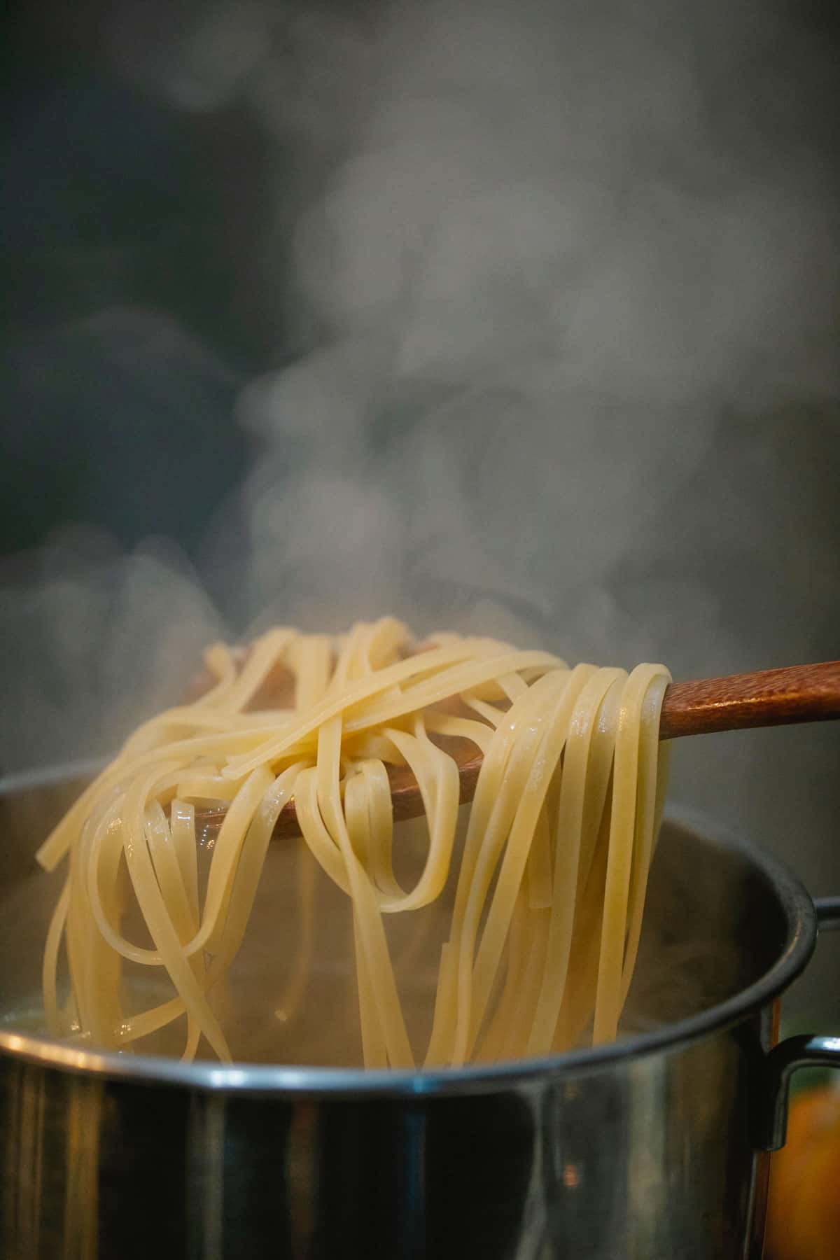 Fettuccine being lifted out of a large pot of boiling water.