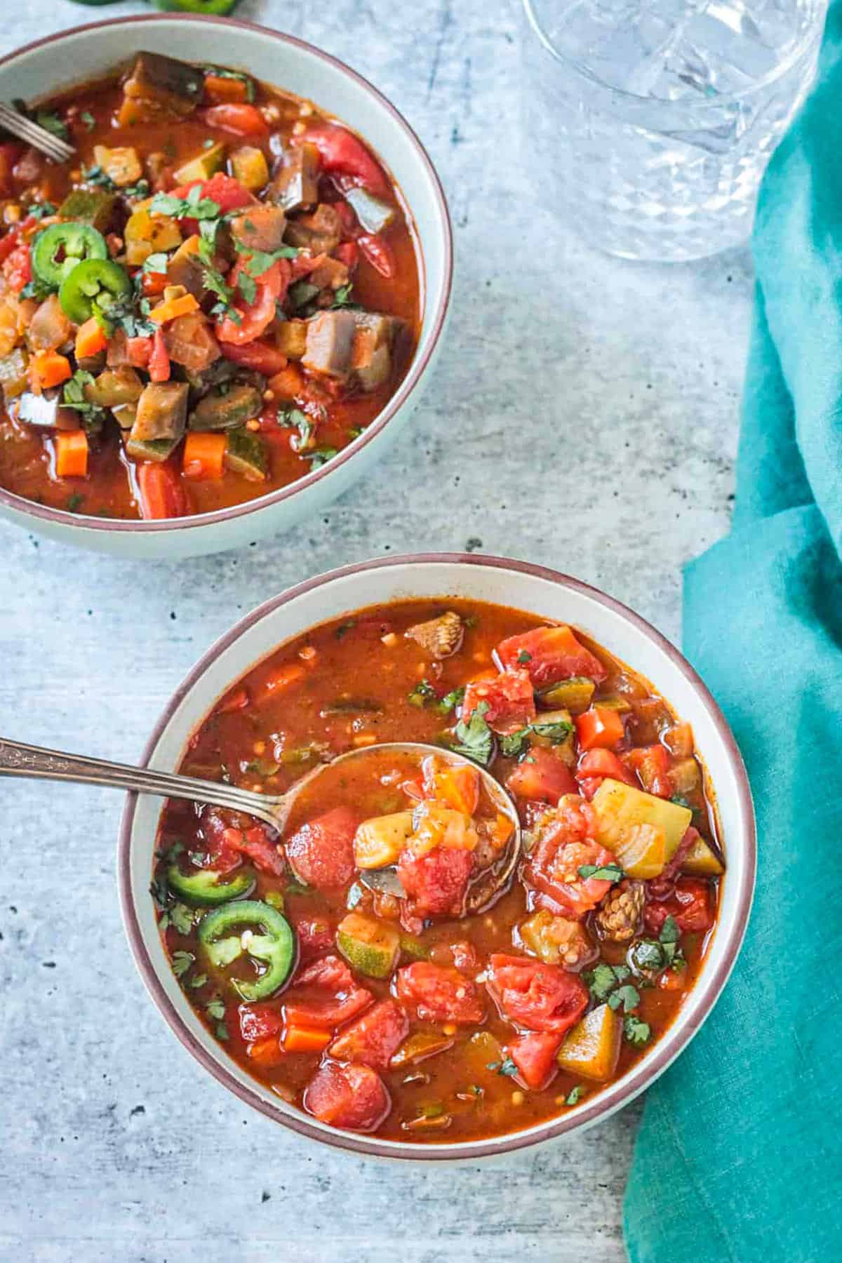 Two bowls of chili soup next to a blue dish cloth.