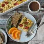 Slice of vegan breakfast casserole on a plate with toast, orange slices, and two forks.