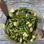 Snap peas, sweet peas, cucumbers, onion, fresh herbs, and dressing mixed in a glass bowl.