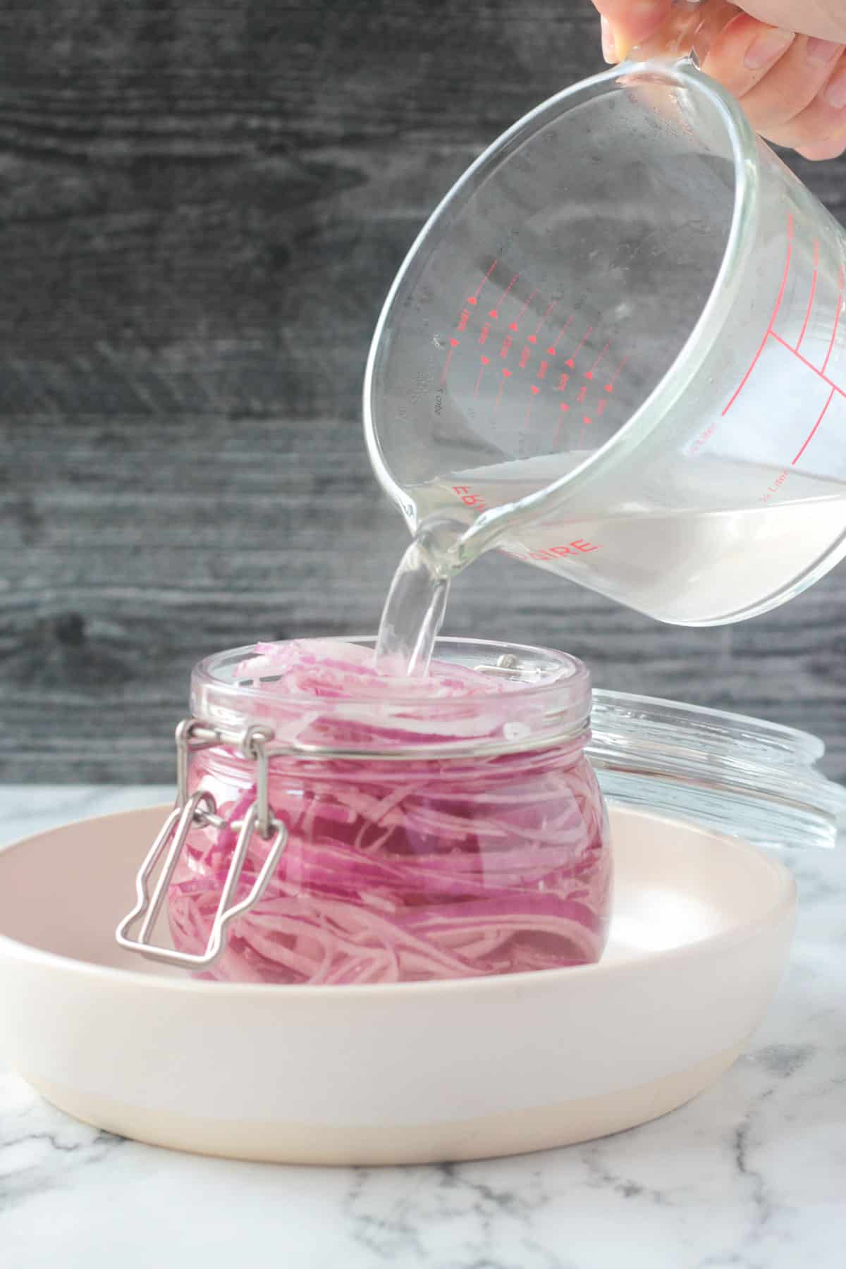 Pouring liquid ingredients into a jar of sliced red onions.