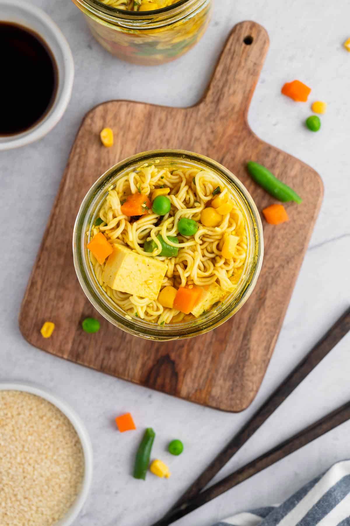 Vegan instant ramen noodles in a glass jar with tofu, carrots and peas.