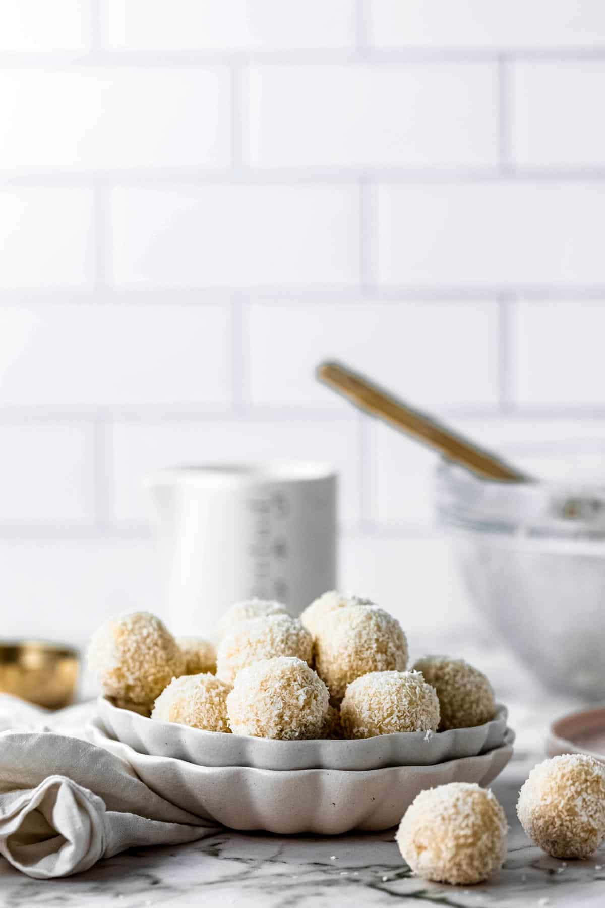 Two coconut bliss balls in front of a bowl of more.