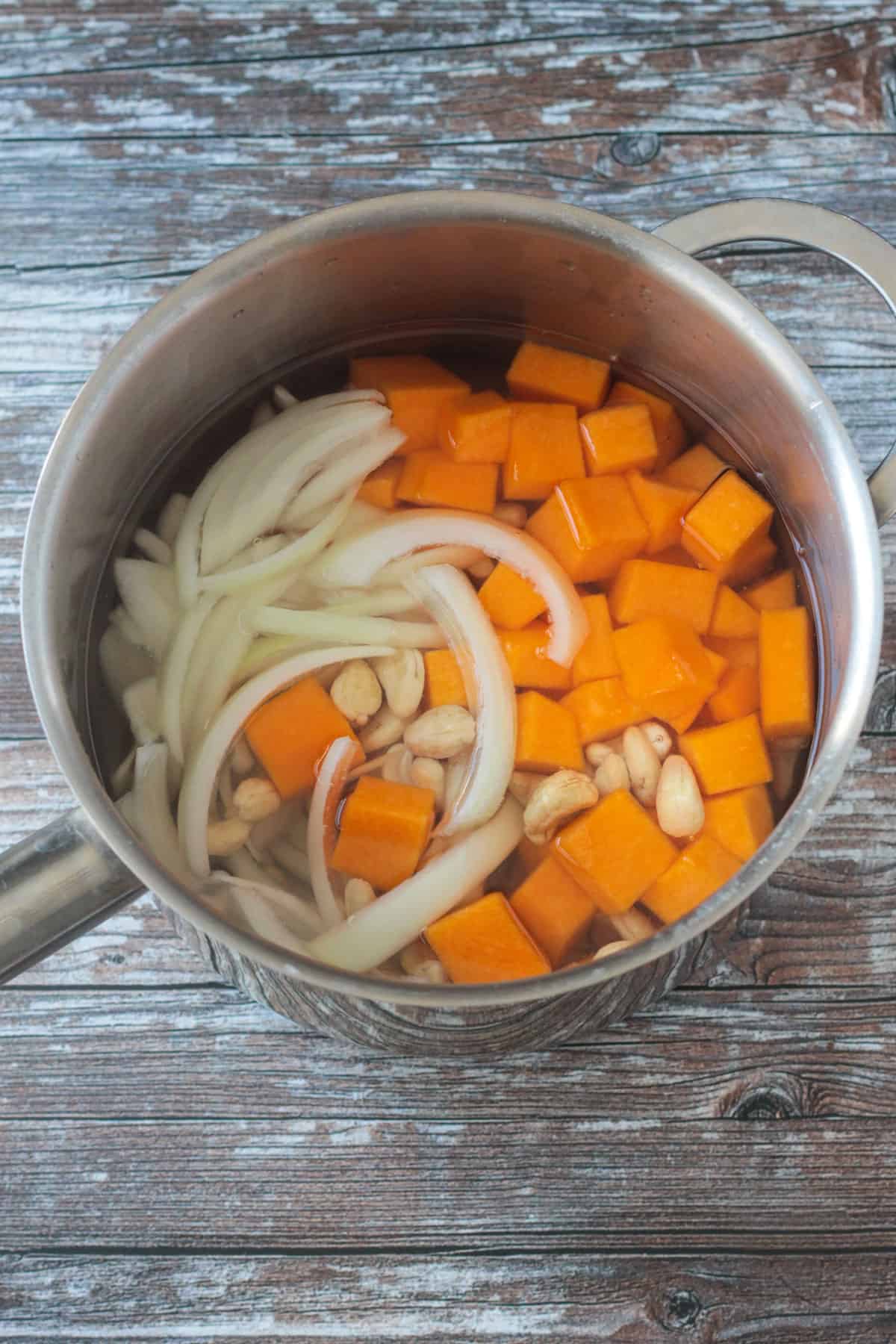 Squash, onions and cashews in a pot of water on the stove.