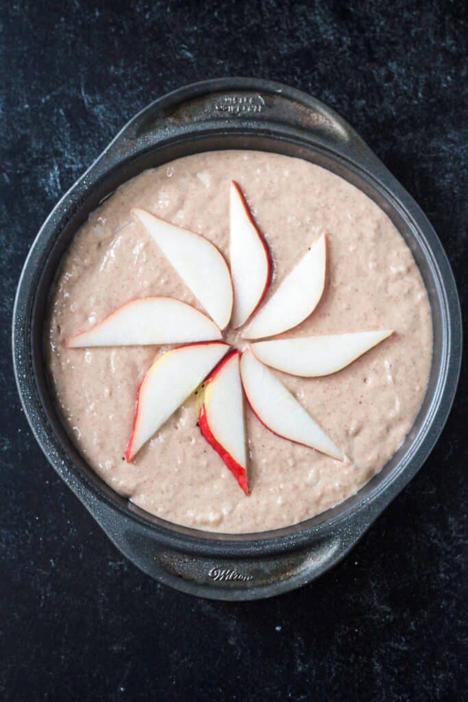 Slices of pear fanned out on top of the cake batter in a pan.