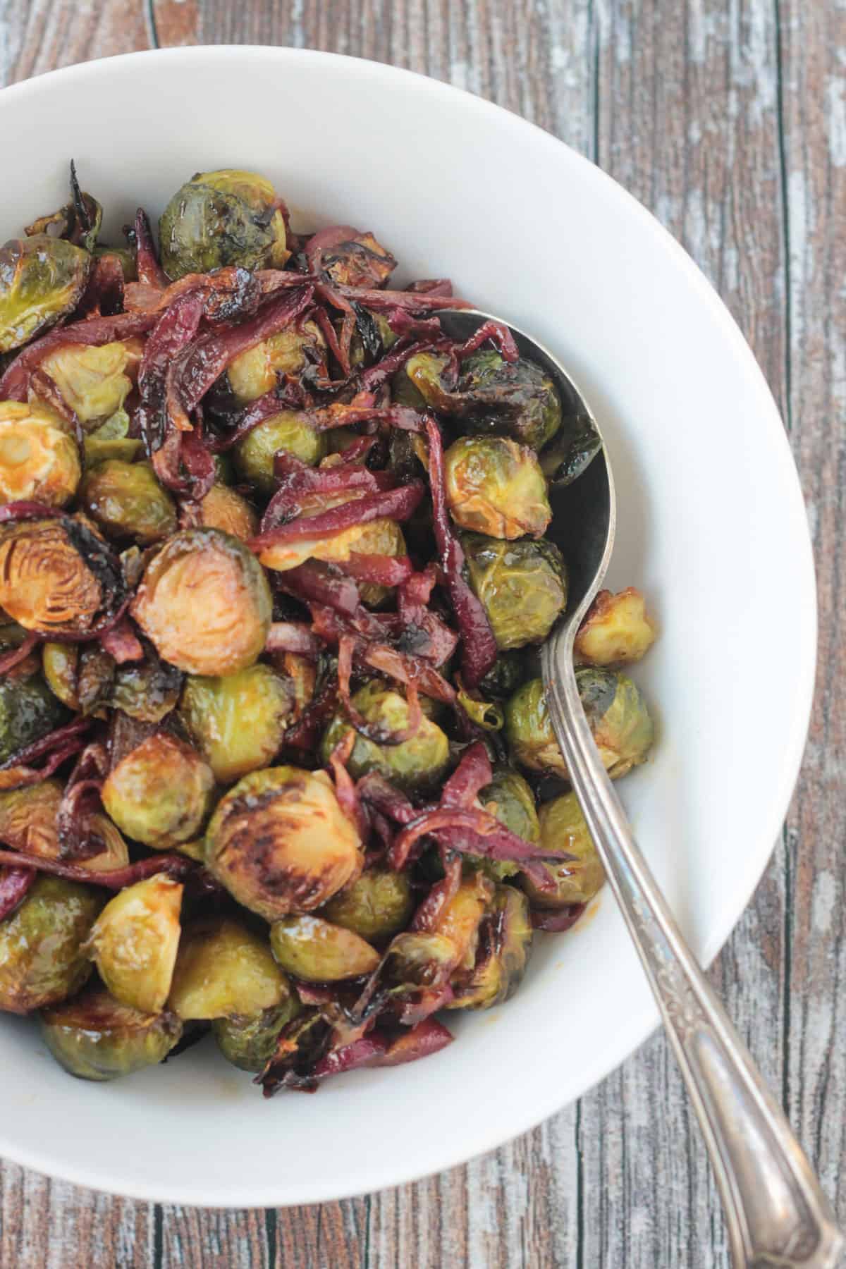 Close up of roasted brussels sprouts on a spoon in a white bowl.