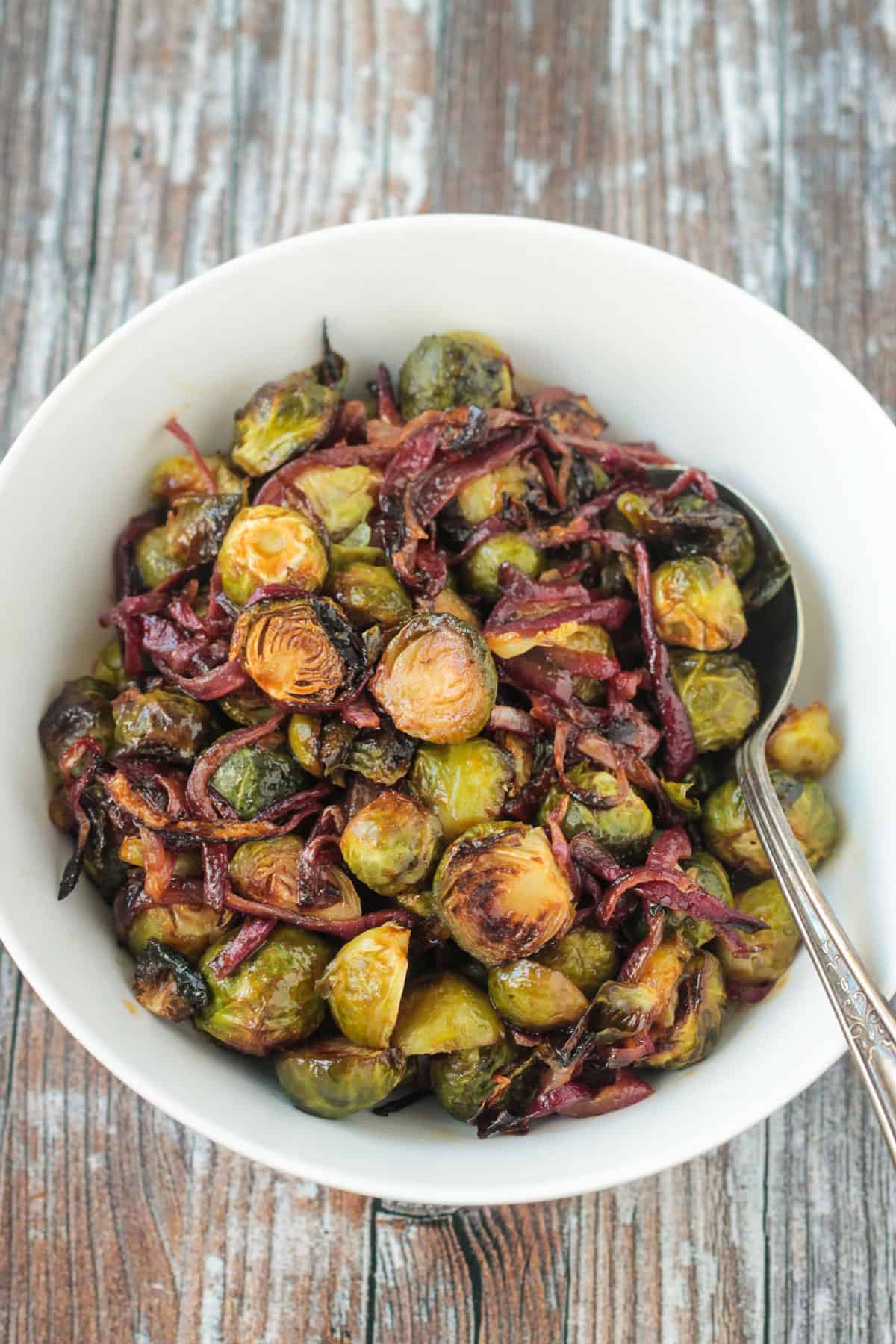 Balsamic glazed roasted sprouts and onions in a white serving bowl.