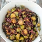 Balsamic glazed roasted sprouts and onions in a white serving bowl.