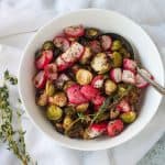 Roasted radishes and brussels sprouts in a white bowl with a serving spoon.