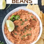 Bowl of vegan refried beans garnished with a lime wedge and surrounded by tortilla chips.