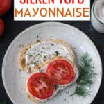 Two halves of toast topped with mayonnaise spread, tomato slices, and fresh dill.