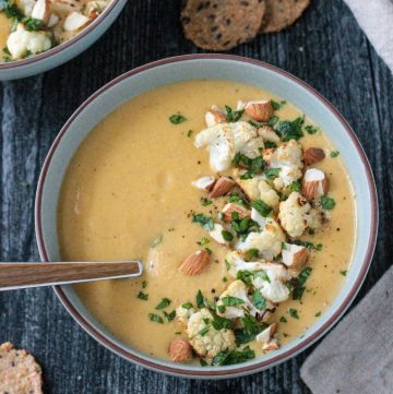 Bowl of creamy vegan cauliflower soup topped with roasted cauliflower and sliced almonds.