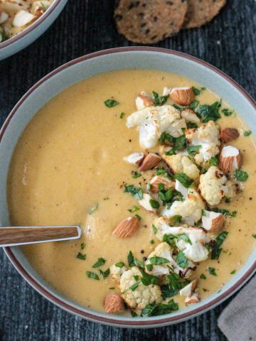 Bowl of creamy vegan cauliflower soup topped with roasted cauliflower and sliced almonds.