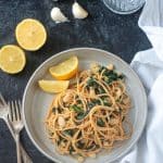 Spaghetti past with white beans kale on a gray plate with two lemon wedges.