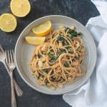 Spaghetti past with white beans kale on a gray plate with two lemon wedges.