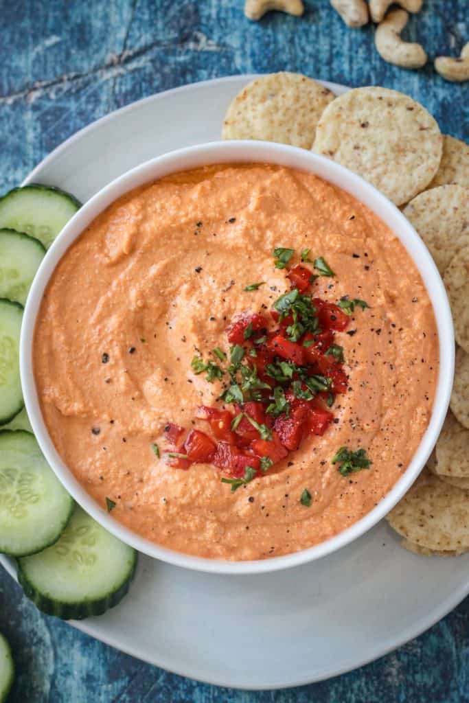 Close up overhead view of cashew dip topped with diced roasted red peppers and chopped fresh parsley.