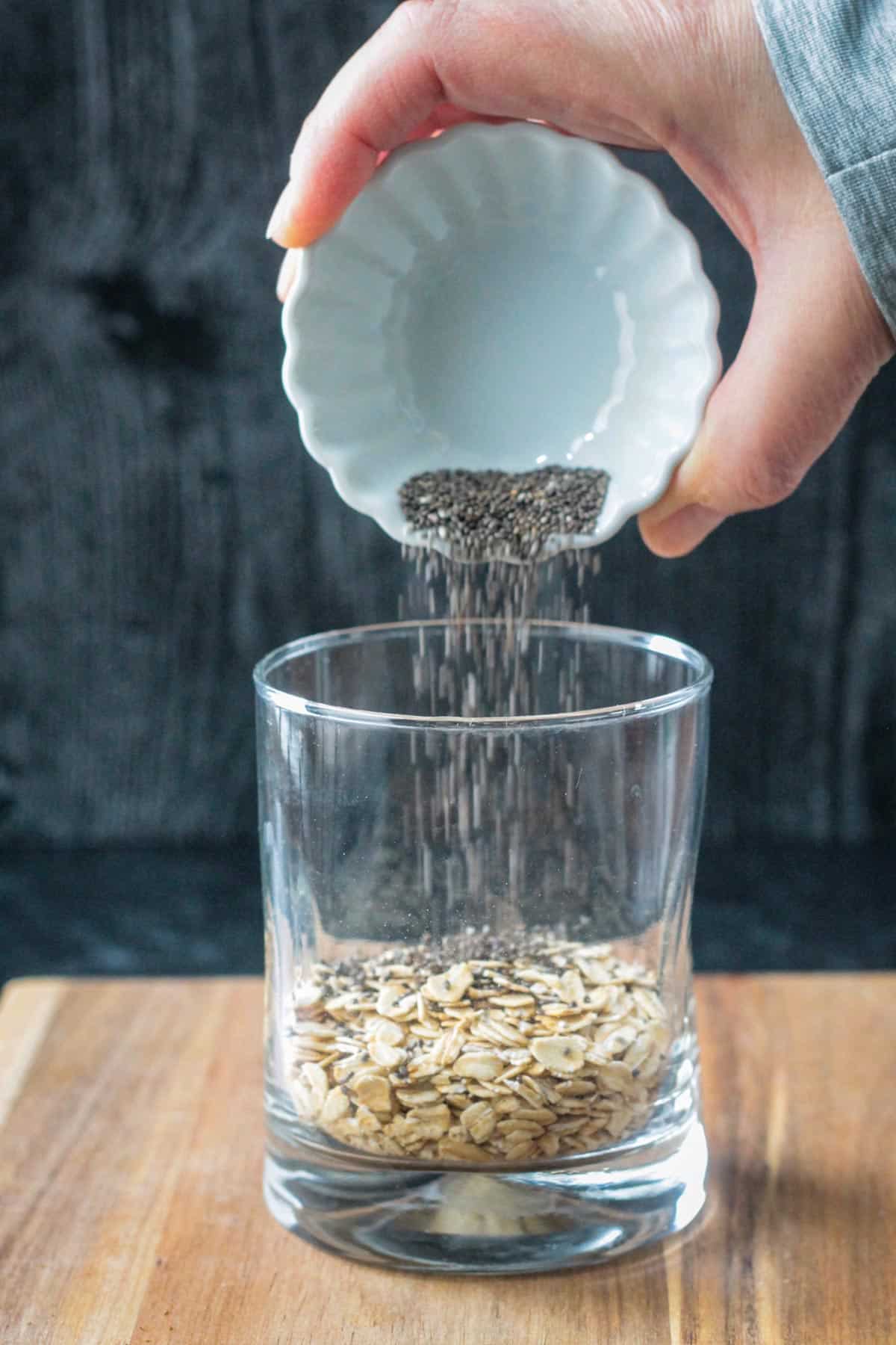 Pouring chia seeds into the glass on top of oats.