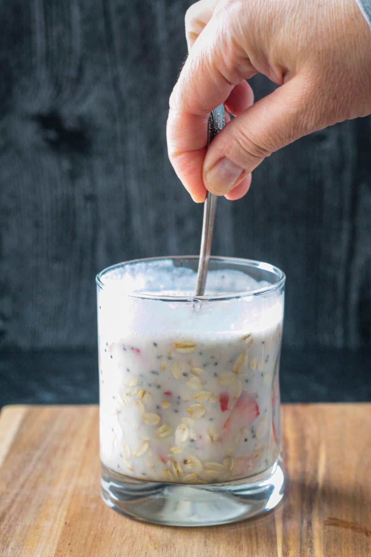 Stirring the overnight oats with coconut milk in a glass.