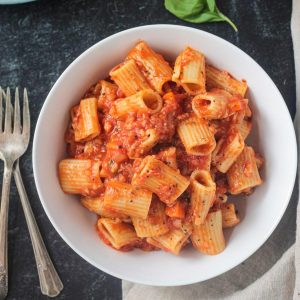 Rigatoni noodles with vegan cauliflower bolognese in a white bowl.