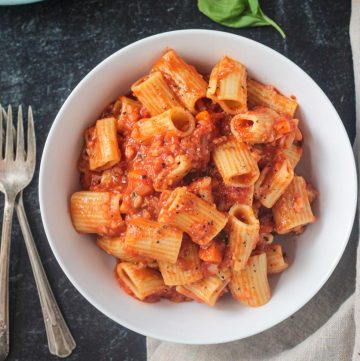 Rigatoni noodles with vegan cauliflower bolognese in a white bowl.