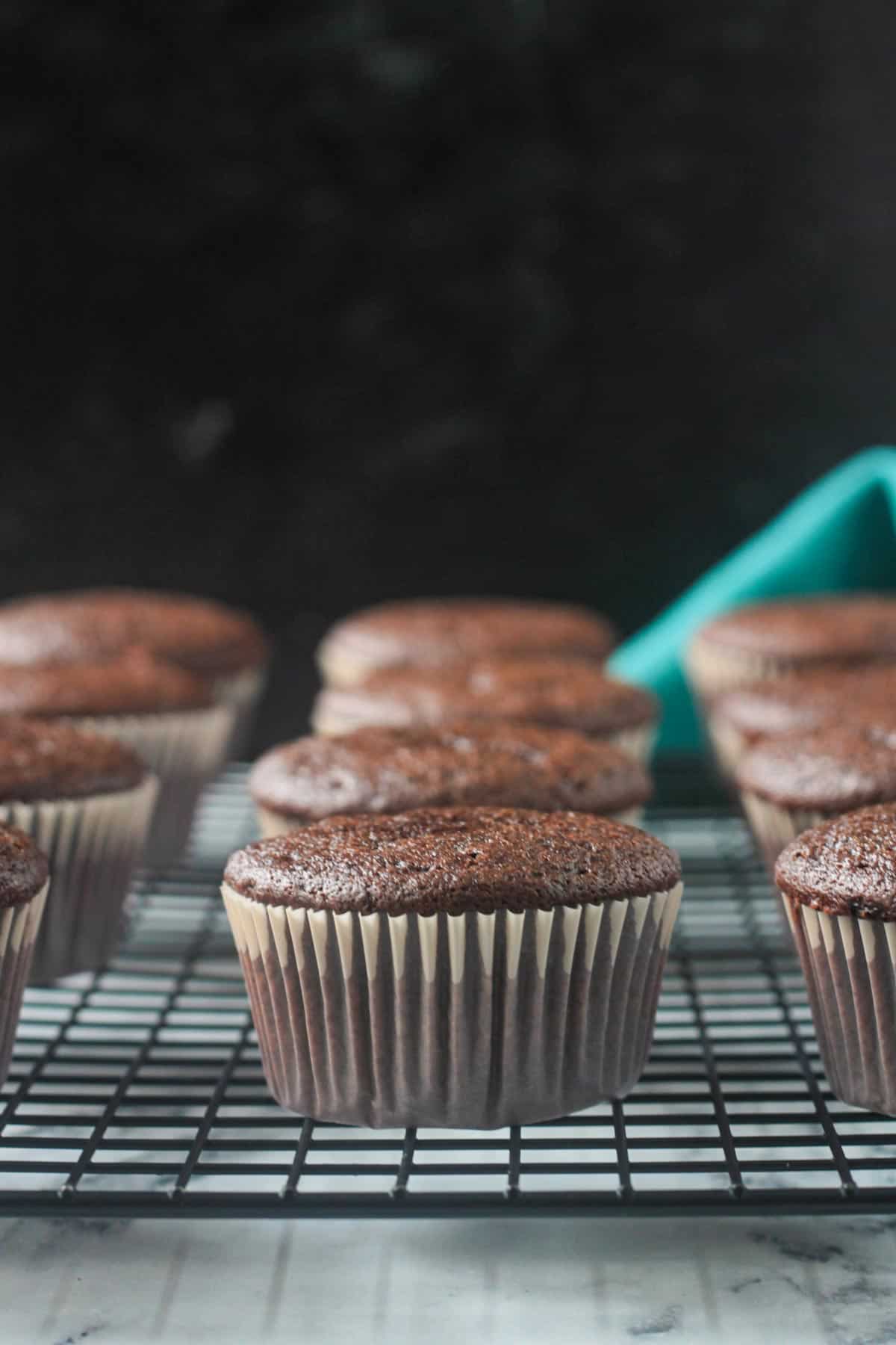 Close up of one finished chocolate cupcake in a cupcake liner on a cooling rack.