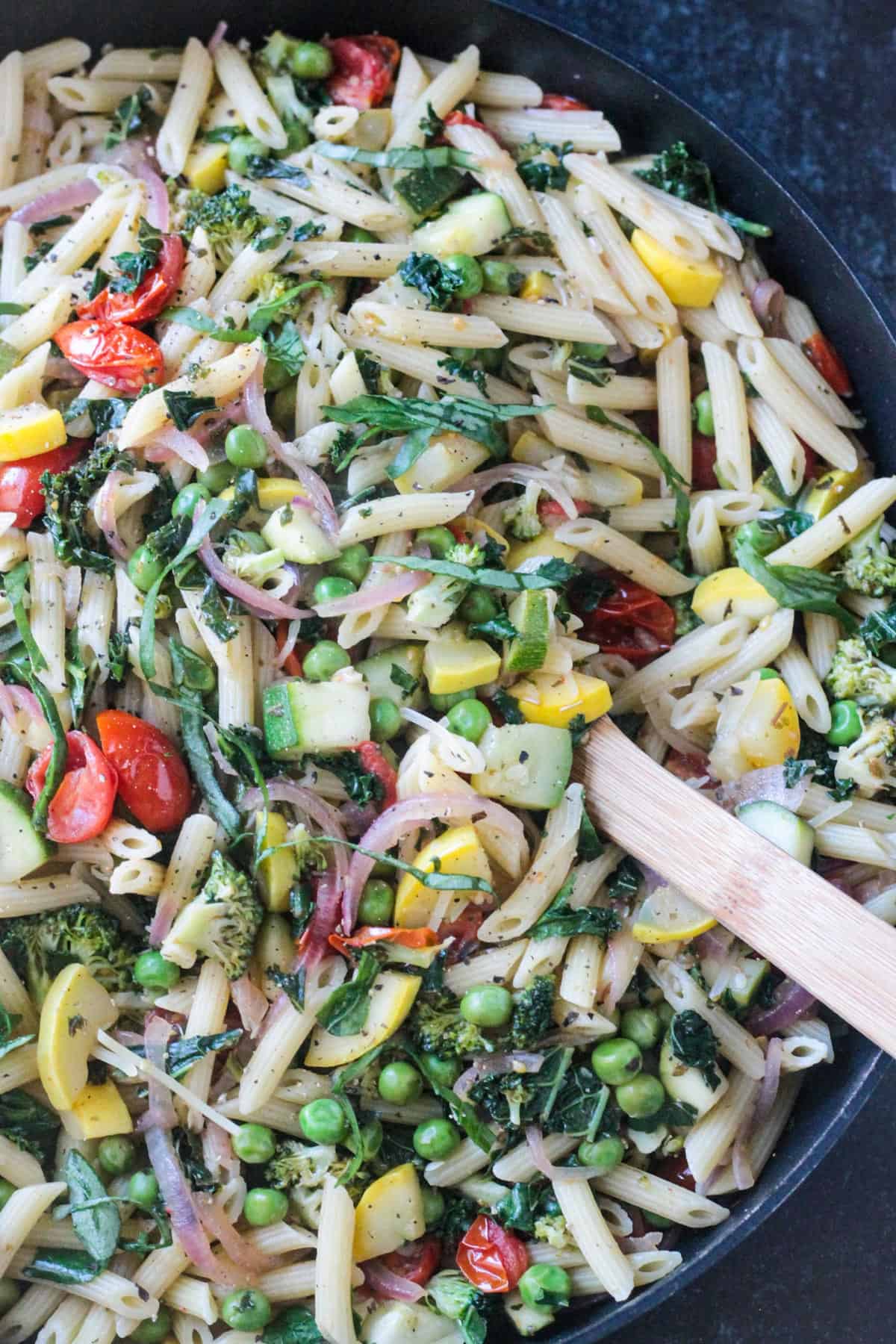 Close up of a variety of vegetables mixed with penne pasta.